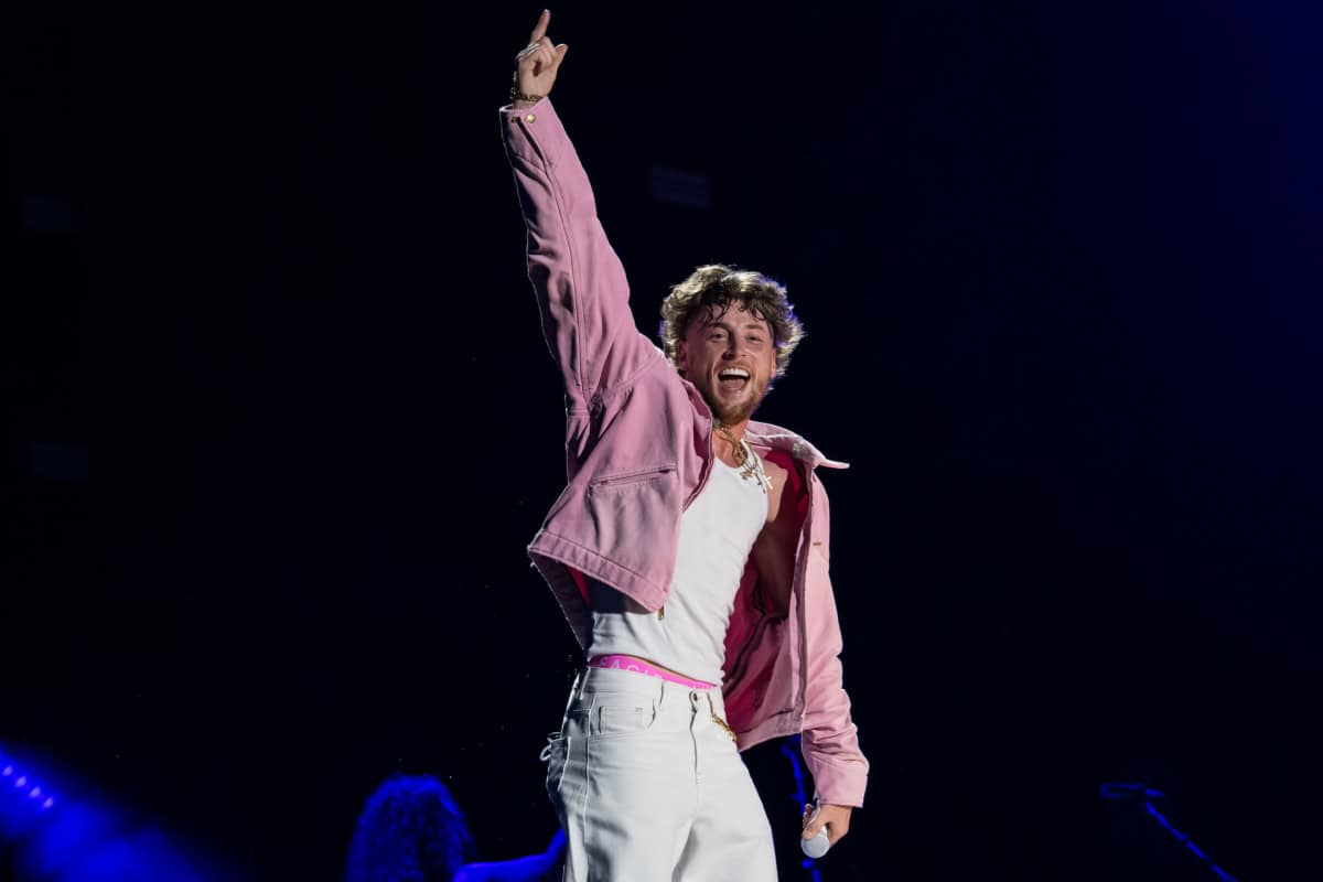 Bailey Zimmerman performing on stage with a pink jacket and raised hand.